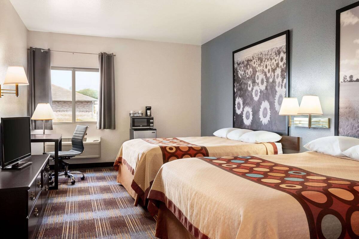 A hotel room with two beds, a desk, a chair, a TV, and a window with curtains.