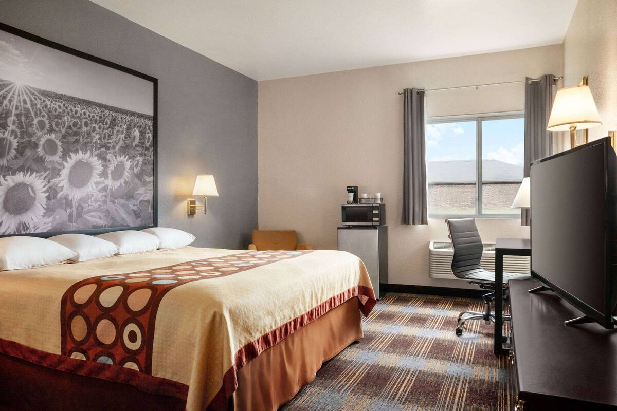 A hotel room with a large bed, a desk with a computer, a chair, a TV, and a window with curtains.