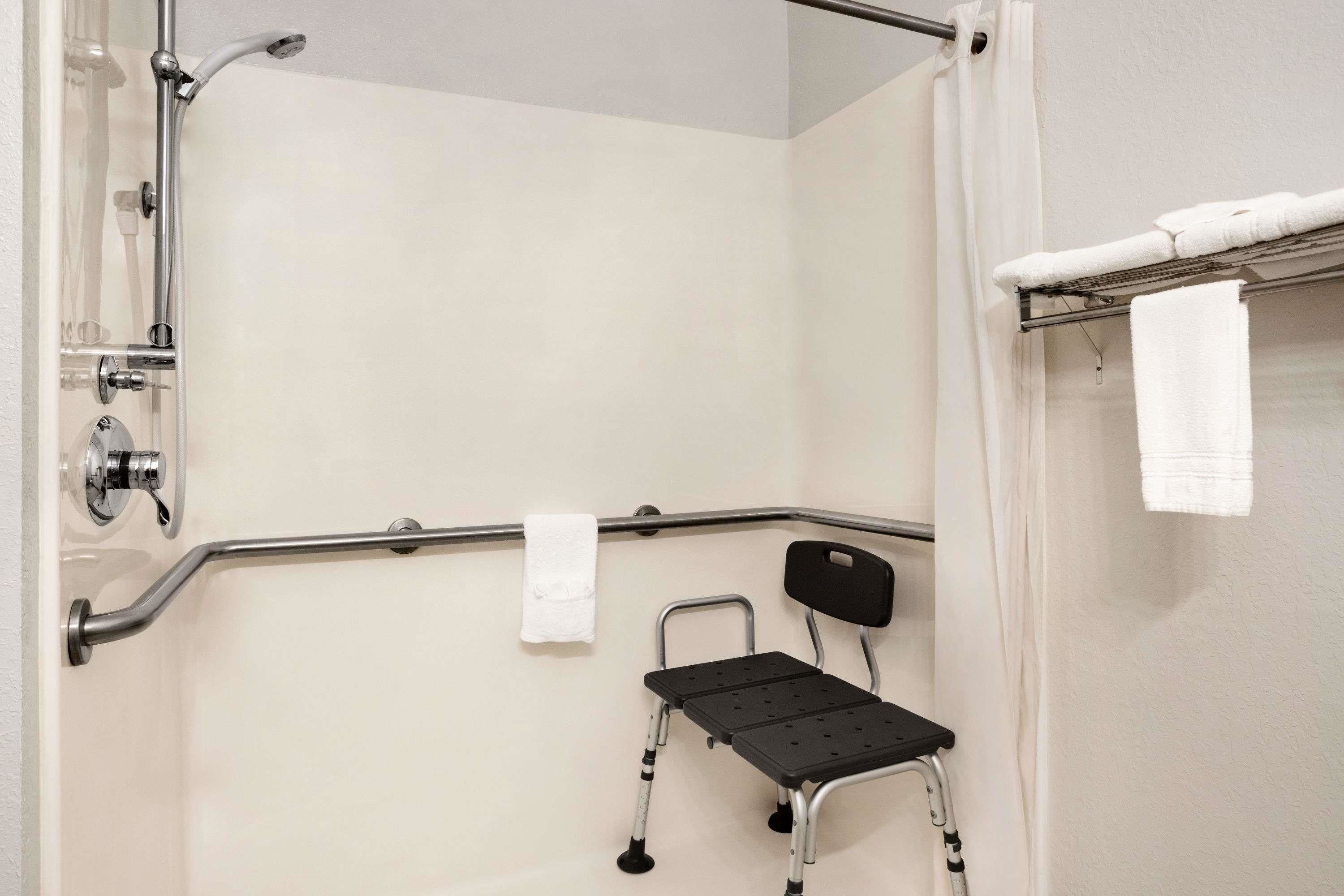 Un baño con ducha, barras de apoyo, una silla de ruedas y un perchero para toallas.
