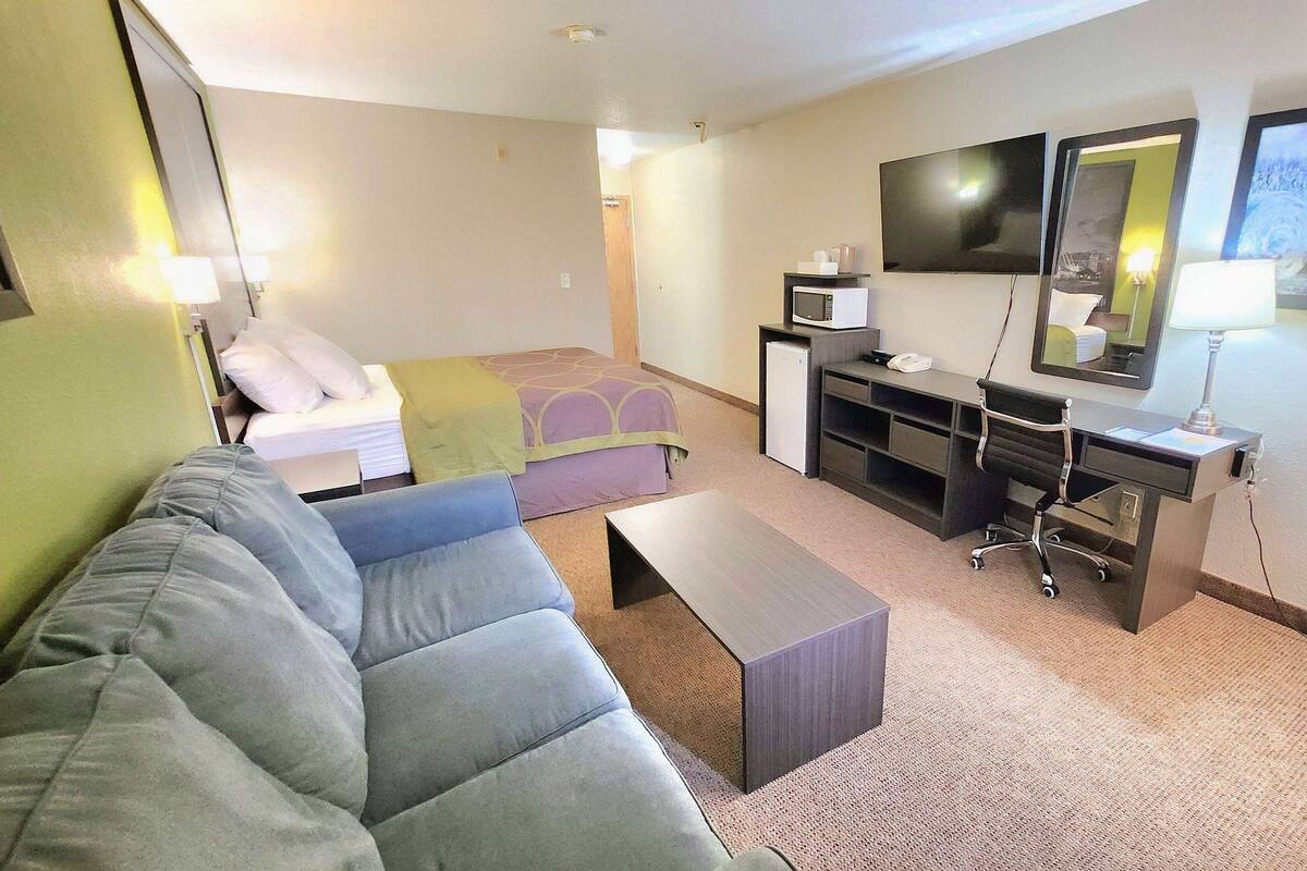 A hotel room with a sofa, a bed, a desk, a TV, and a mirror.