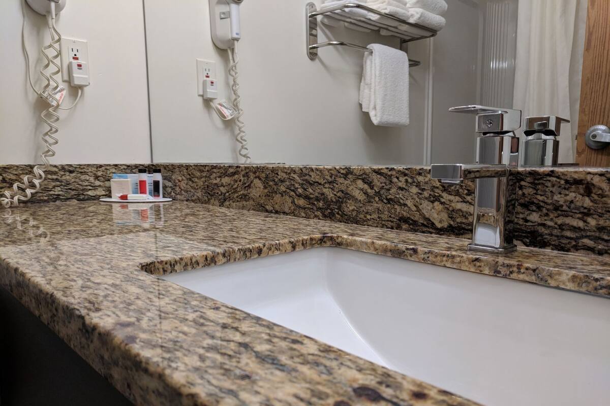 A bathroom with a granite countertop, a sink, a towel rack, and a mirror.