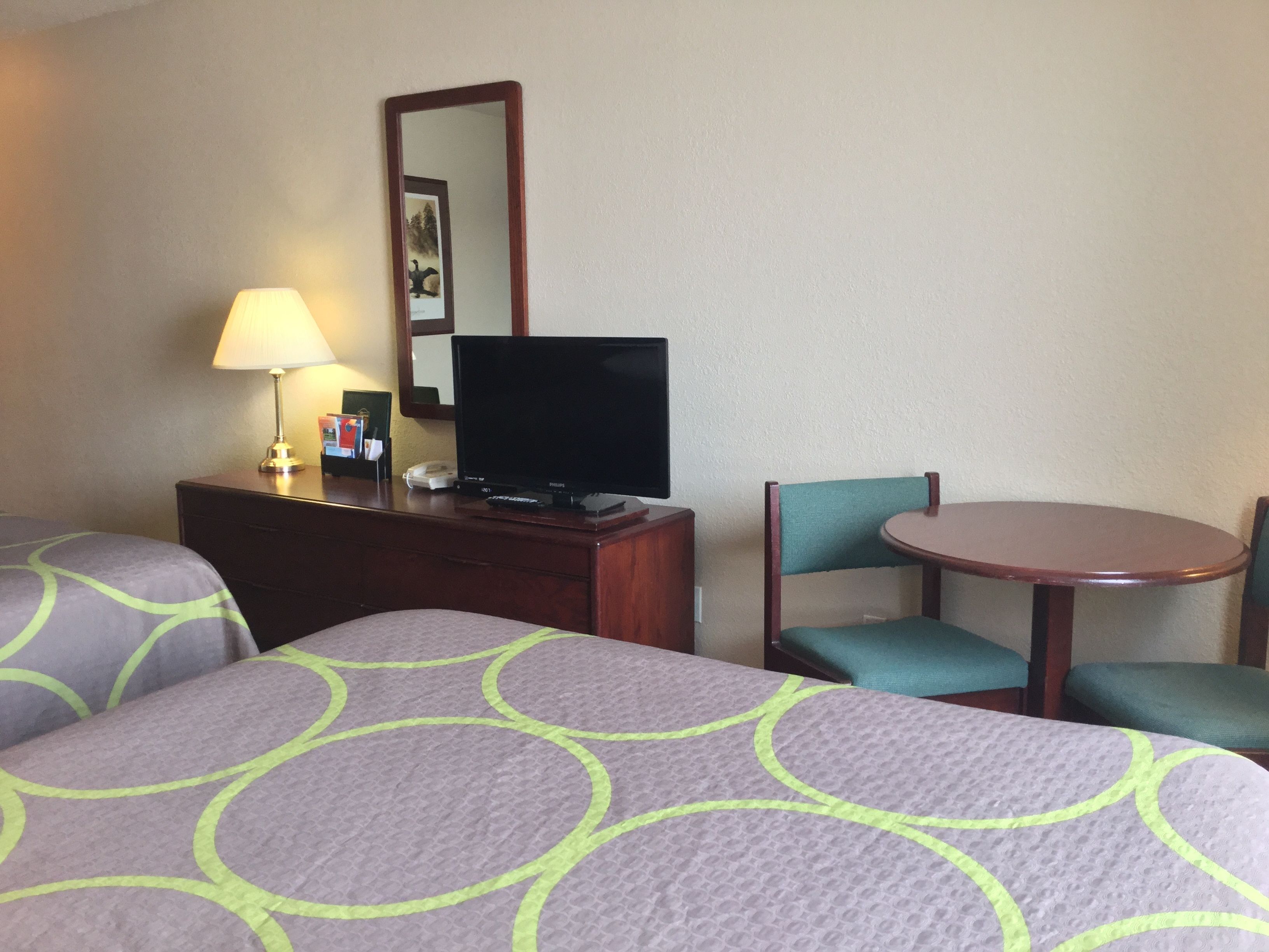 A hotel room with two beds, a desk with a television, a lamp, and a chair.