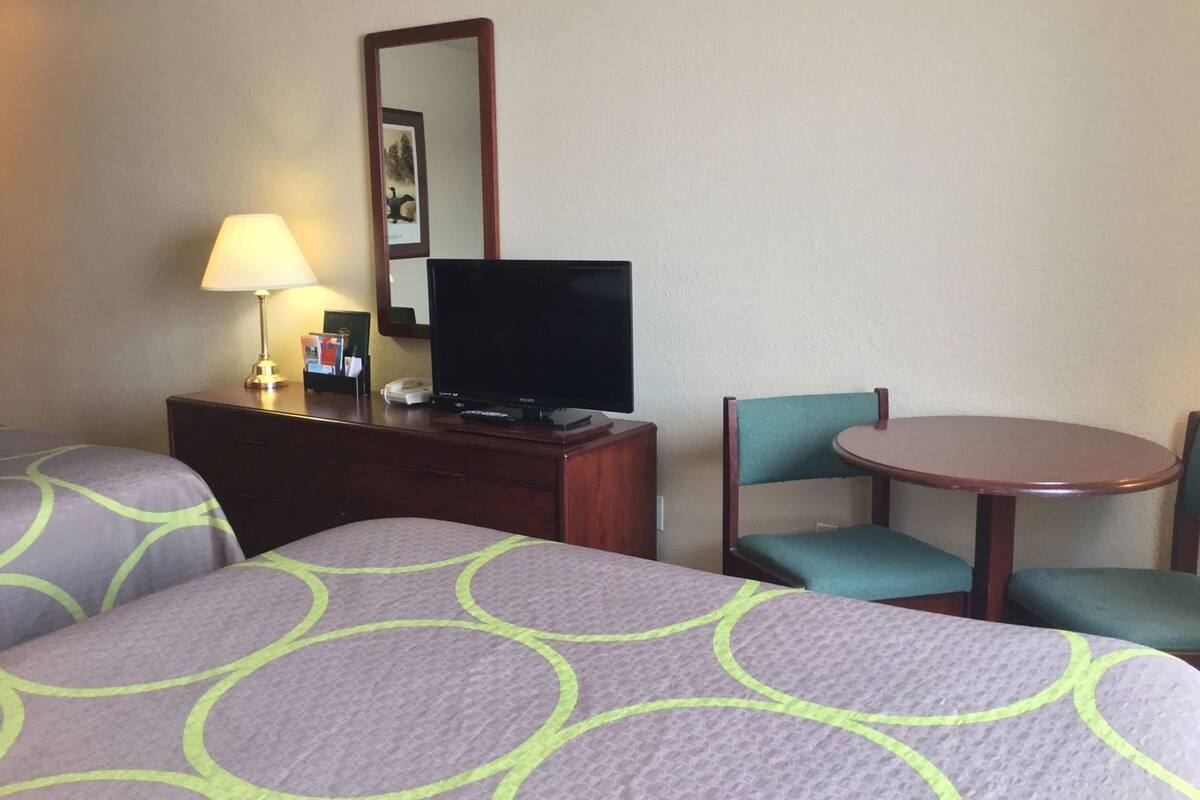 A hotel room with two beds, a desk with a television, a lamp, and a chair.