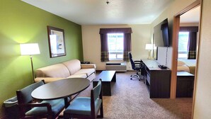 A hotel room with a green wall, a sofa, a dining table with chairs, a TV, and a desk. - Super 8 by Wyndham Portage La Prairie MB (Portage La Prairie)