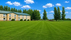 A hotel with a green roof, multiple windows, and a well-maintained lawn. - Super 8 by Wyndham Portage La Prairie MB (Portage La Prairie)
