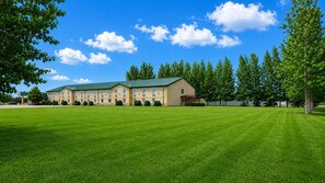 A large building with multiple windows and a green roof, surrounded by a well-maintained lawn and trees. - Super 8 by Wyndham Portage La Prairie MB (Portage La Prairie)