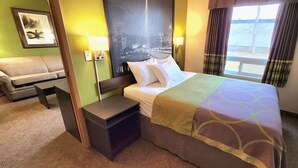 A hotel room with a bed, a nightstand, a desk, a chair, and a view of a cityscape through the window. - Super 8 by Wyndham Portage La Prairie MB (Portage La Prairie)