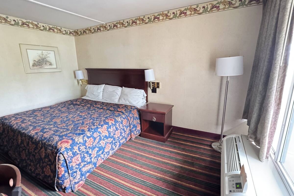 A hotel room with a large bed, two bedside tables with lamps, a framed picture on the wall, and a window with curtains.