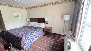 Een hotelkamer met een groot bed, twee nachtkastjes met lampen, een ingelijst schilderij aan de muur en een raam met gordijnen.