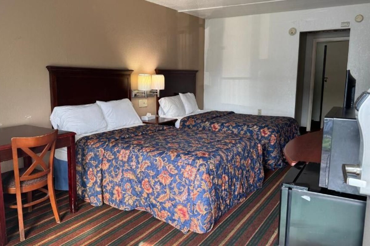 Habitación de hotel con cama, escritorio, silla, televisor y refrigerador.