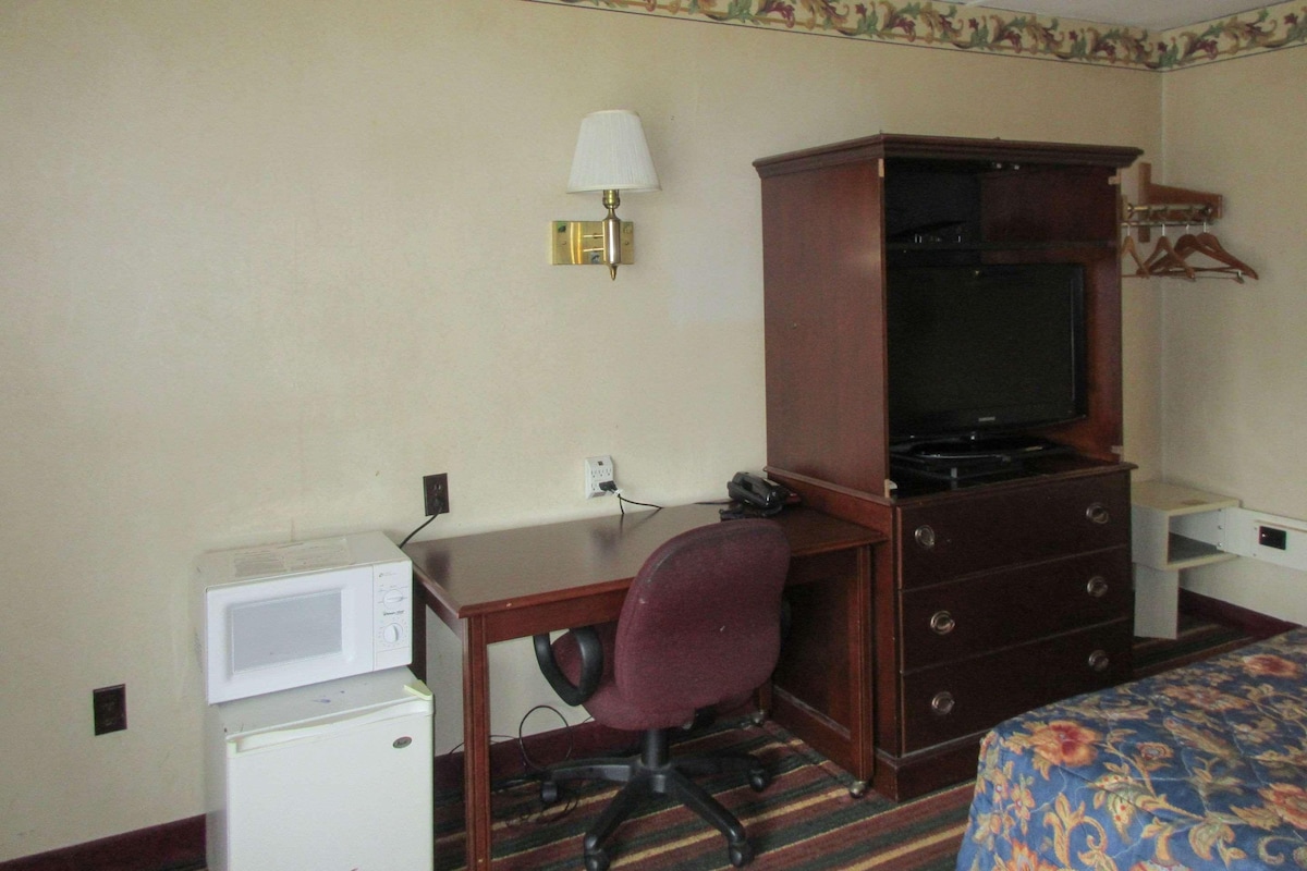 Habitación de hotel con escritorio, televisor, microondas, teléfono y cama con colcha estampada.