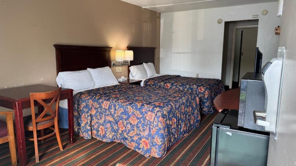 A hotel room with a bed, a desk, a chair, a TV, and a refrigerator.