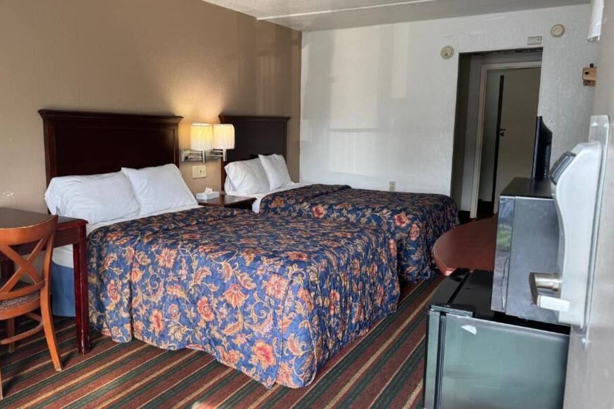 A hotel room with a bed, a desk, a chair, a TV, and a refrigerator.