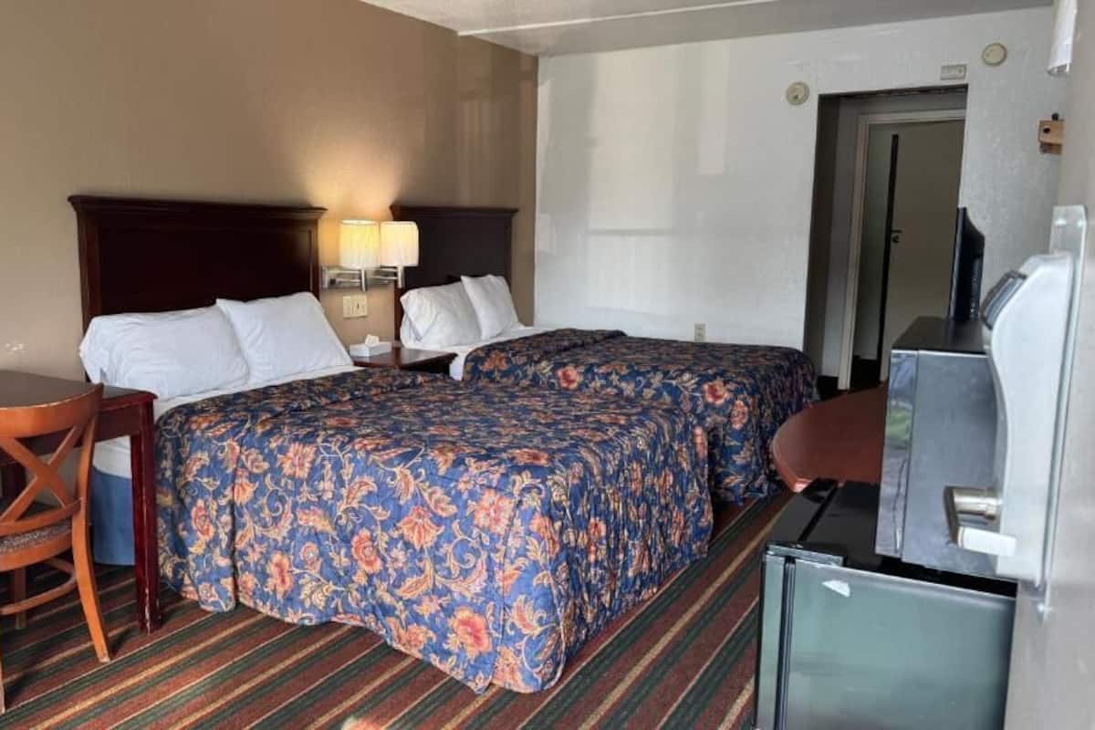 Quarto de hotel com cama, escrivaninha, cadeira, televisão e frigorífico.