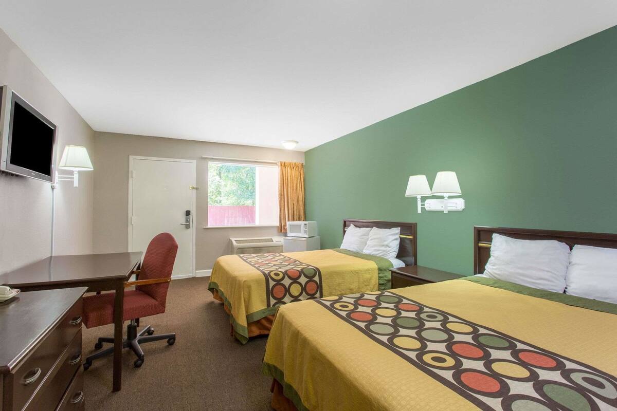 Ein Hotelzimmer mit zwei Betten, einem Schreibtisch, einem Stuhl, einem Fernseher und einem Fenster mit Vorhängen.