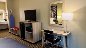 Une chambre d’hôtel comprenant un lit, un bureau avec une chaise, une télévision, un four à micro-ondes et un miroir.