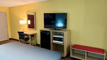 Una habitación de hotel con una cama, un escritorio con lámpara, un televisor, un microondas y un banco.
