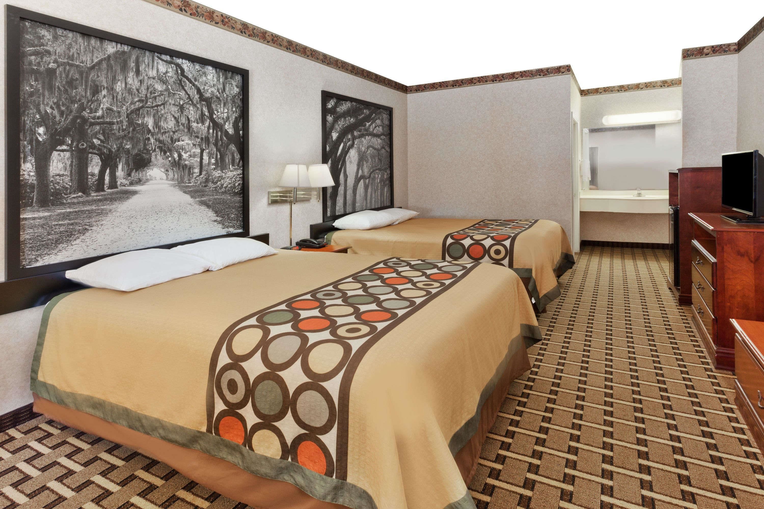 A hotel room with two beds, a television, a bathroom, and a large window with a view of trees.