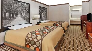 A hotel room with two beds, a television, a bathroom, and a large window with a view of trees.