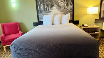 Habitación de hotel con una cama grande, un sillón rojo, una mesita de noche con lámpara y un teléfono en la pared.