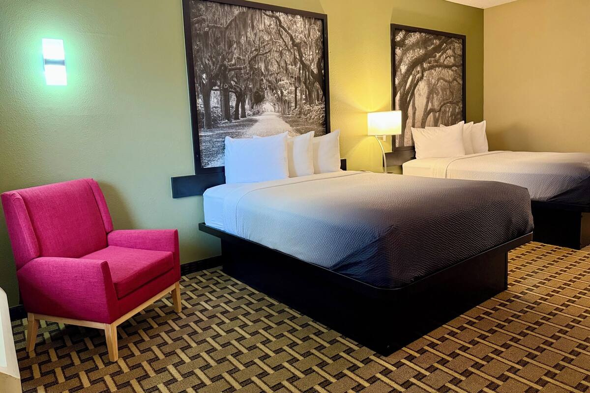 Una habitación de hotel con dos camas, una silla rosa y una alfombra estampada.