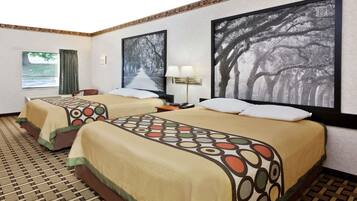 A hotel room with two beds, each with a patterned bedspread, a large window with curtains, and two framed pictures on the wall.