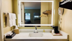 Une salle de bain avec un lavabo blanc, un miroir avec un éclairage intégré, un porte-serviettes, un téléphone et une fenêtre donnant sur l’extérieur.