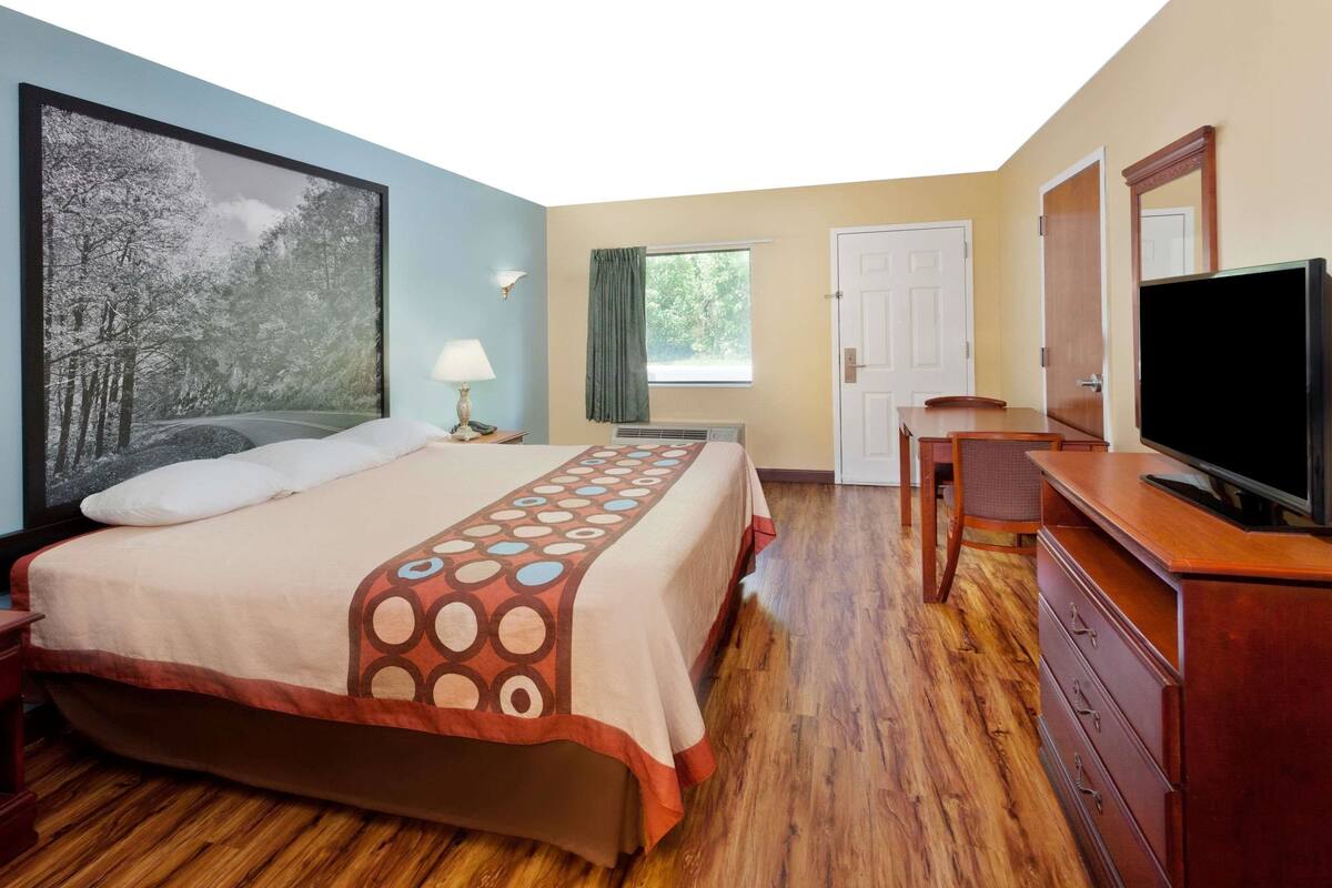 Una habitación de hotel con cama, televisión, escritorio, silla, ventana y puerta.