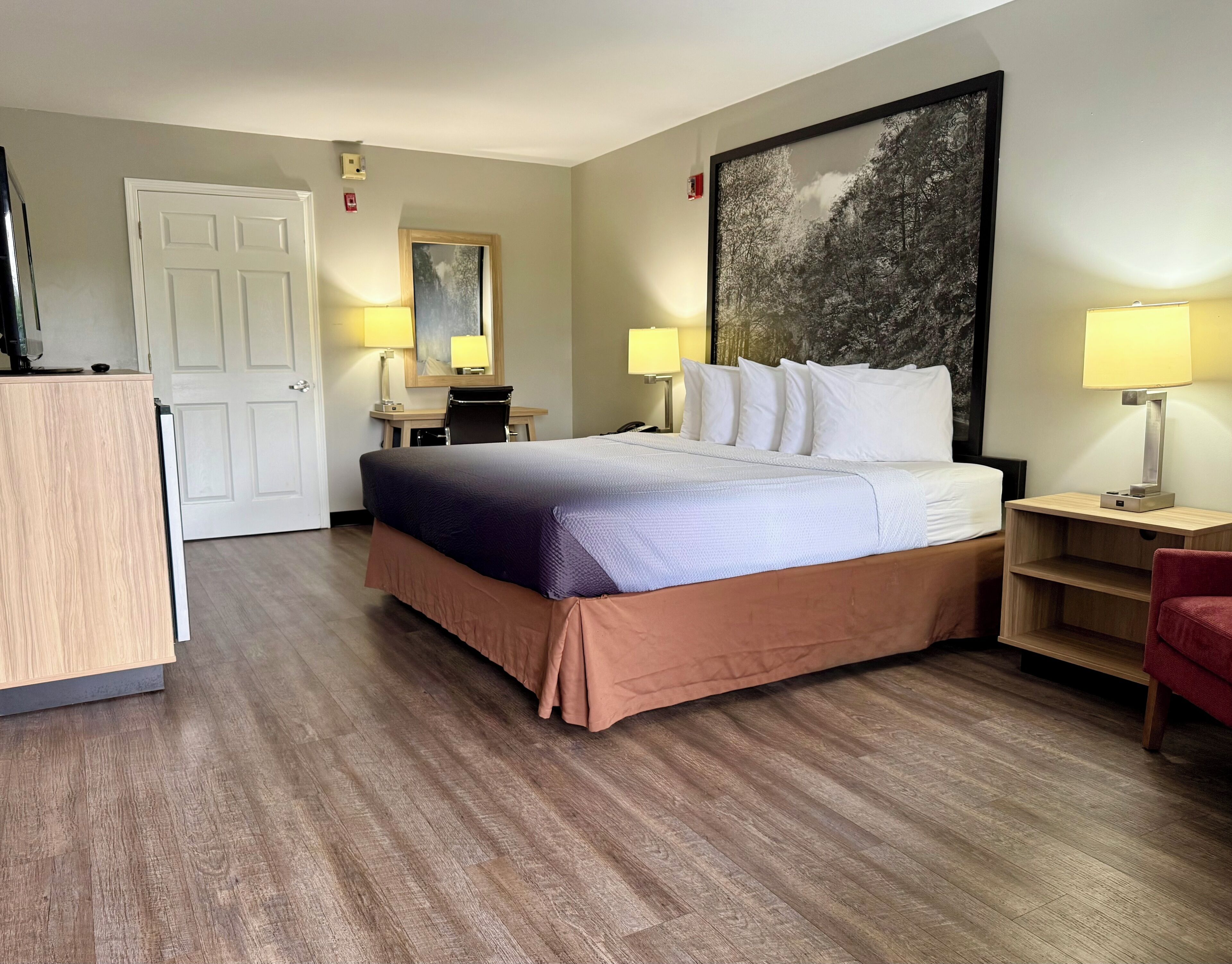 A hotel room with a bed, desk, chair, and two bedside lamps.