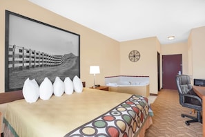 Une chambre d’hôtel avec un grand lit, un bureau, une chaise, une lampe de bureau, un téléviseur fixé au mur, un grand tableau encadré et une salle de bain avec une baignoire et des toilettes.