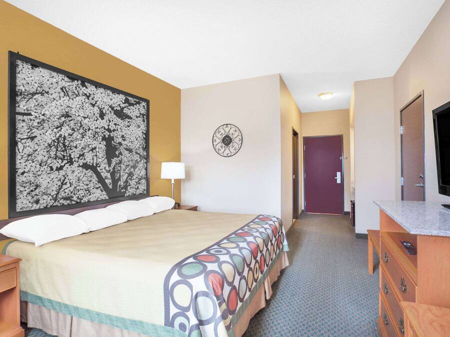 Une chambre d’hôtel avec un grand lit, une télévision, une commode et une horloge murale.