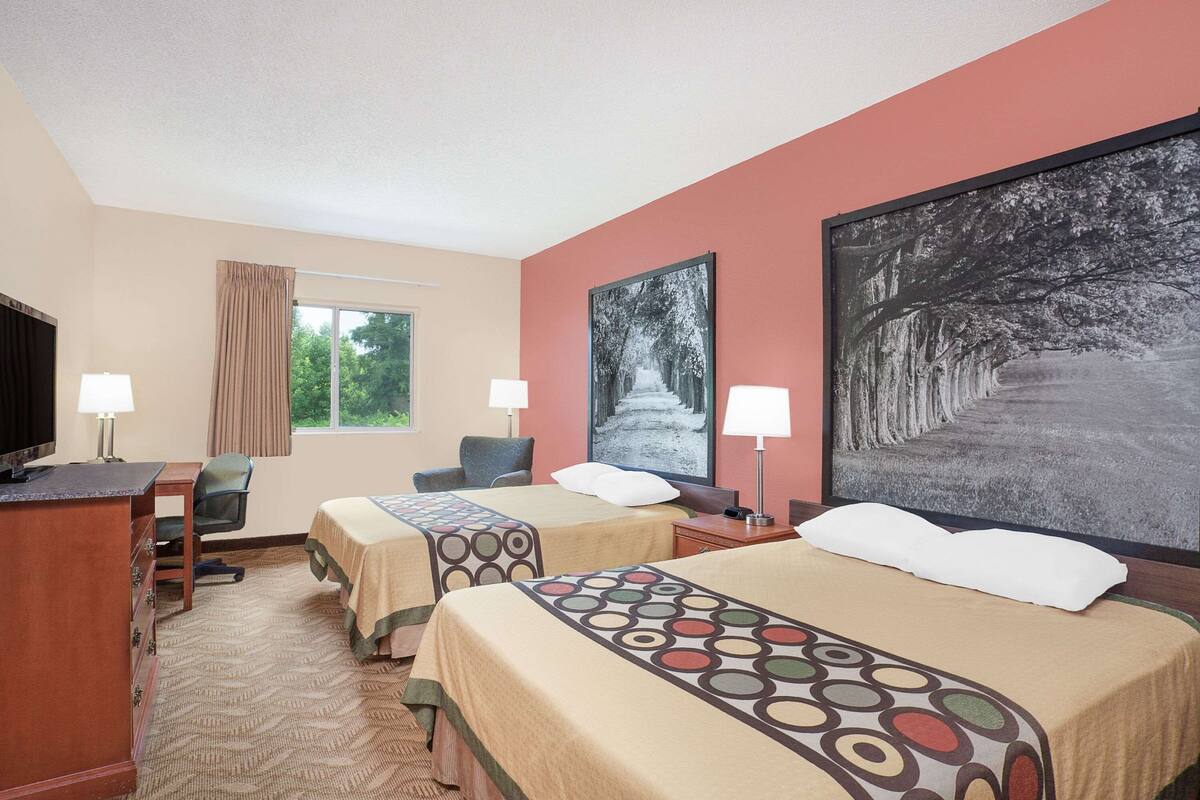 Een hotelkamer met twee bedden, een bureau, een stoel, een televisie en een groot raam.