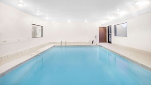 A large indoor swimming pool with a tiled floor, surrounded by walls with windows and doors.