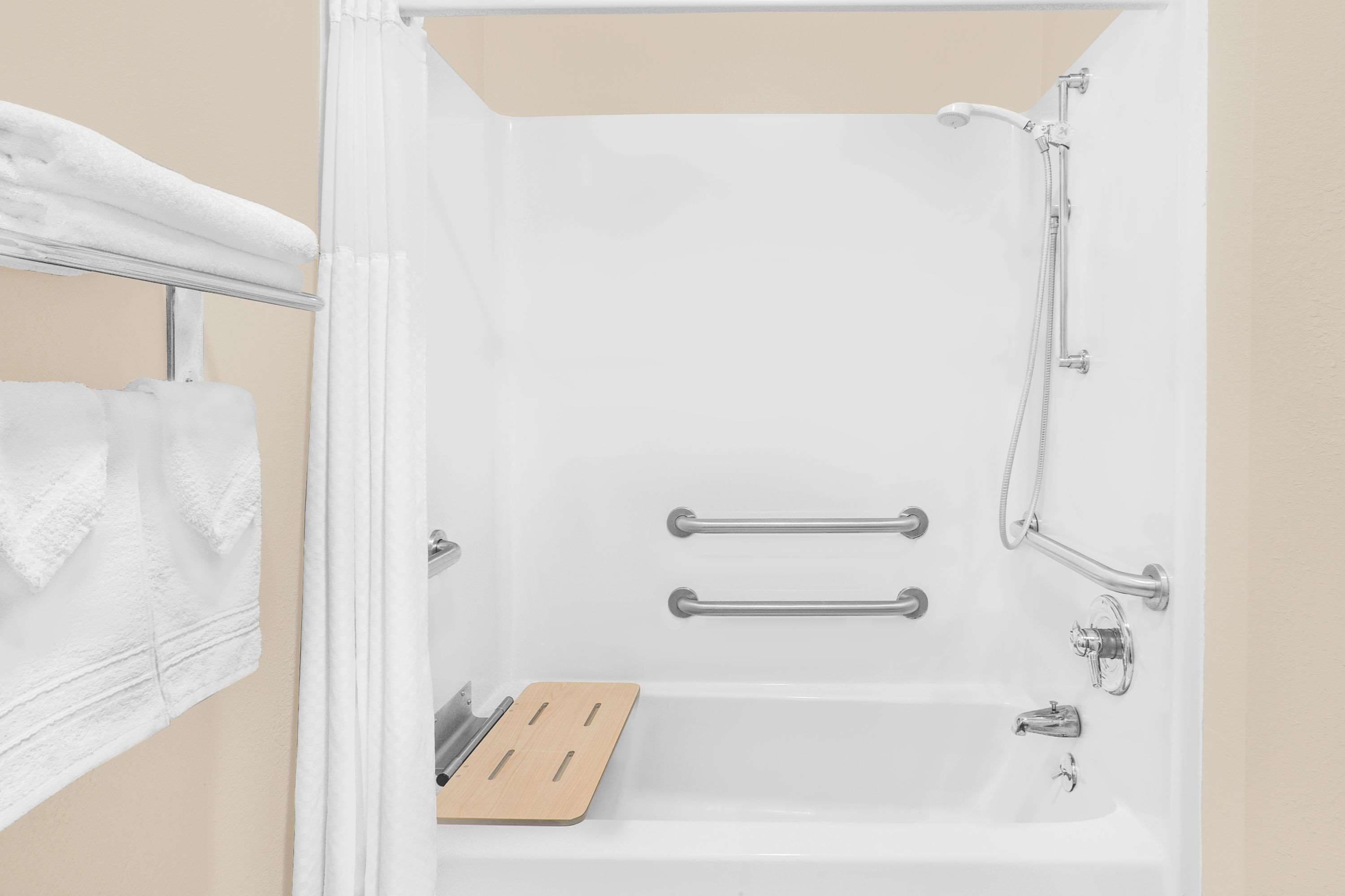 A bathroom with a bathtub, grab bars, a showerhead, and a towel rack.