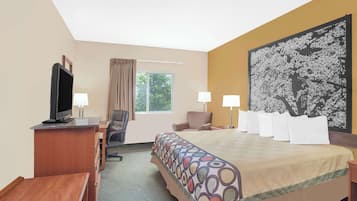 A hotel room with a bed, a desk with a TV, a chair, a window with curtains, and a large floral painting on the wall.