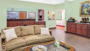 A living room with a beige sofa, a coffee table, and a kitchen area with wooden cabinets and a microwave.