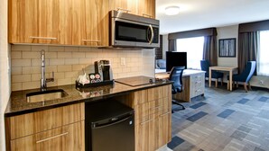 Una cocina compacta con microondas, lavabo y refrigerador, un pequeño comedor con mesa y sillas, y un televisor al fondo.