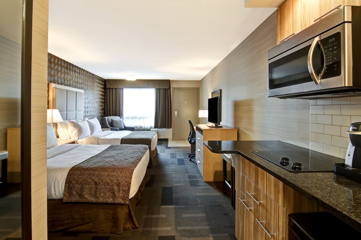 Quarto de hotel com duas camas, cozinha compacta, micro-ondas e televisão.