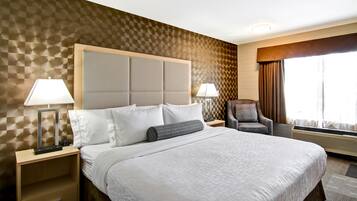 Quarto de hotel com uma cama grande, duas mesas de cabeceira com luminárias, uma cadeira e uma janela com cortinas.