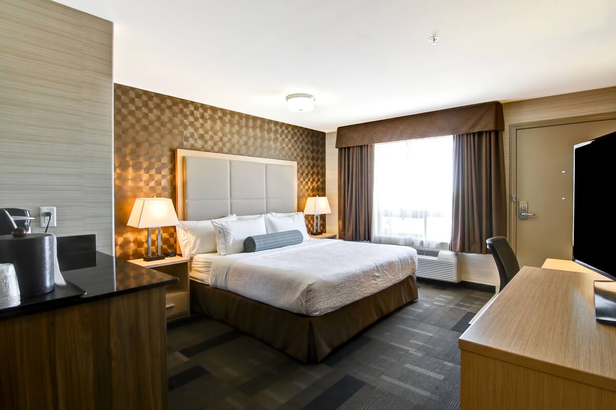 Quarto de hotel com uma cama grande, duas mesas de cabeceira com luminárias, uma escrivaninha, uma cadeira e uma televisão.