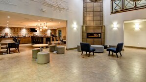 A spacious lobby with a modern design, featuring a central seating area with round tables and chairs, a large fireplace, and decorative ceiling artwork. - Canalta Hotel St Paul (St. Paul)