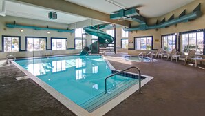 Una piscina interior con tobogán, sillas de descanso y un pequeño jacuzzi.
