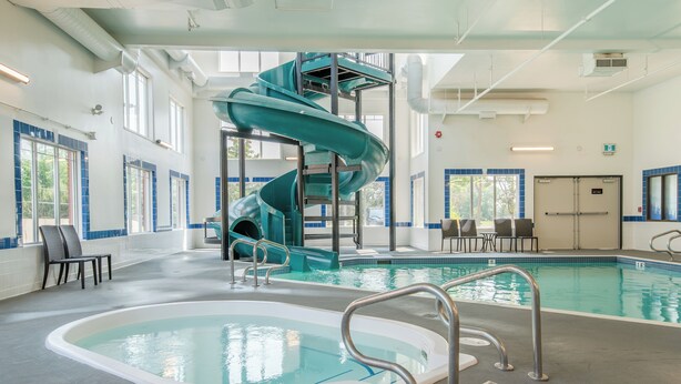 An indoor swimming pool with a spiral slide, seating areas, and a lifeguard station. - Canalta Hotel Cochrane (Cochrane)