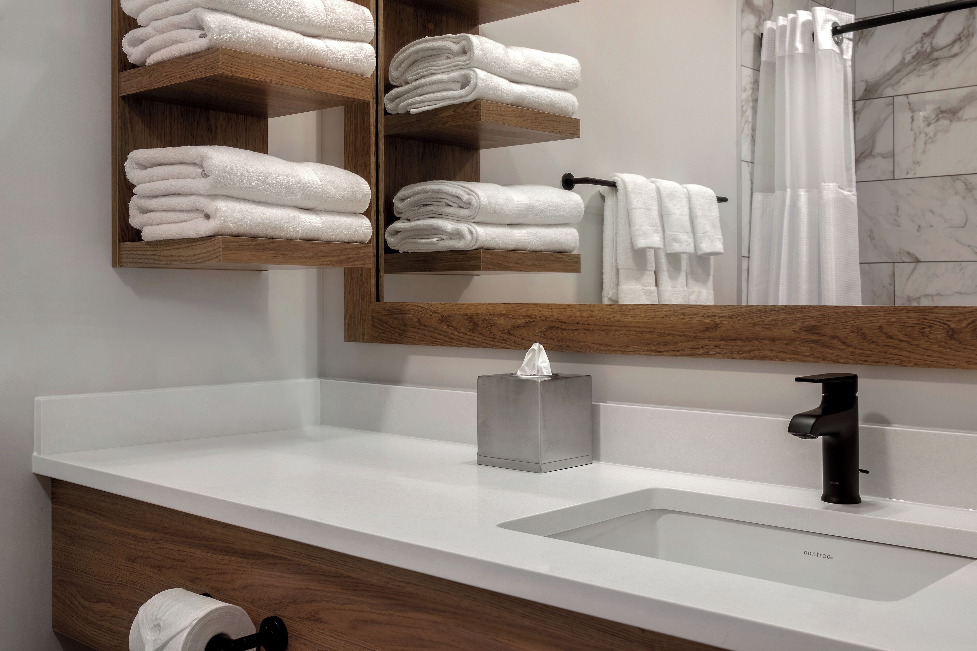 Un baño con lavamanos blanco, un espejo y repisas de madera con toallas dobladas.