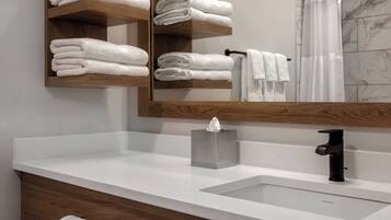 Un baño con lavamanos blanco, un espejo y repisas de madera con toallas dobladas.