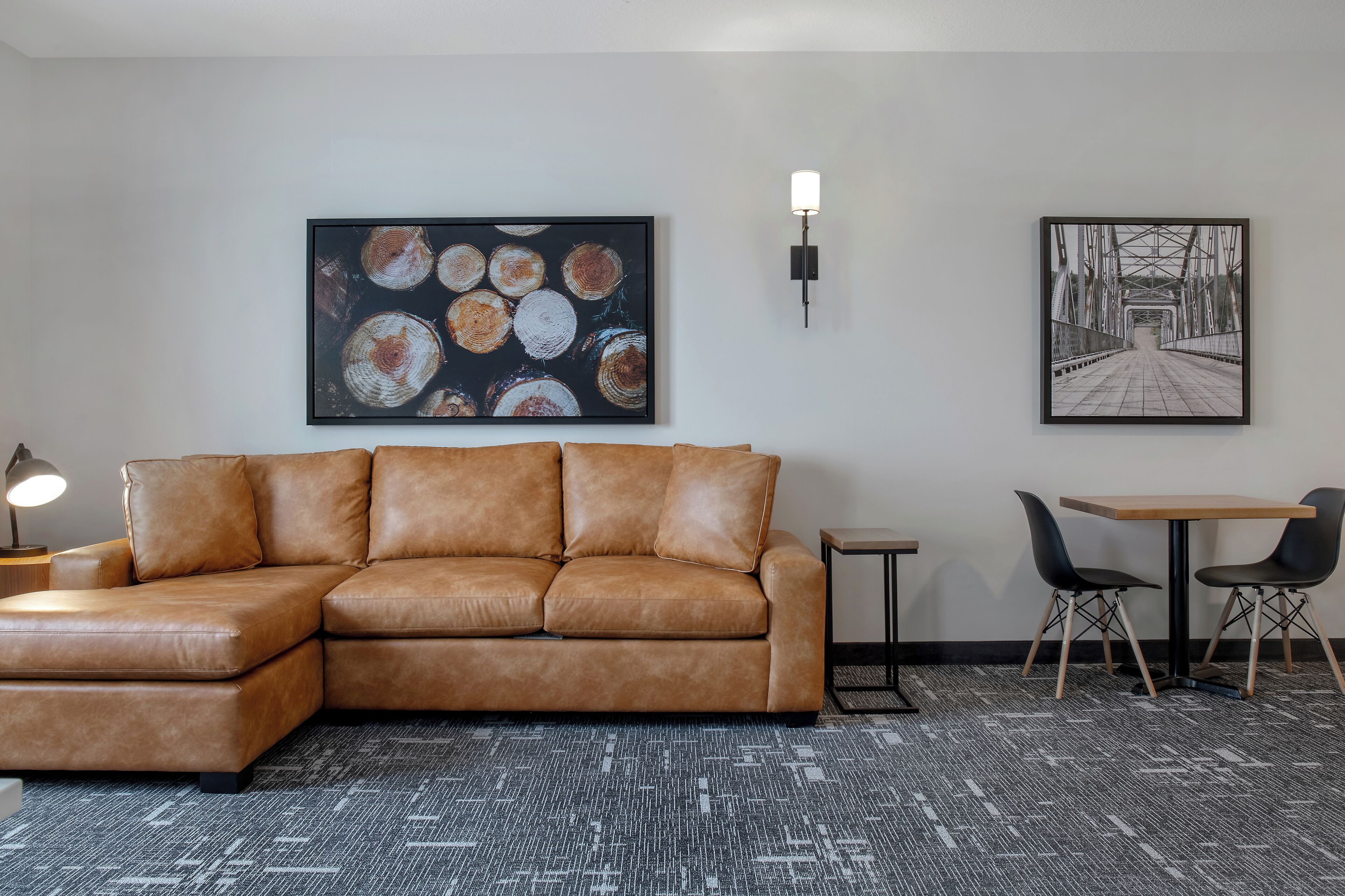 A modern living room with a leather sectional sofa, a small table with two chairs, and two wall-mounted artworks.