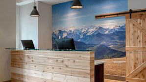 A reception desk with a wooden finish and glass top, laptops on it, and a large mountain view mural in the background. - Canalta Hotel Cochrane (Cochrane)