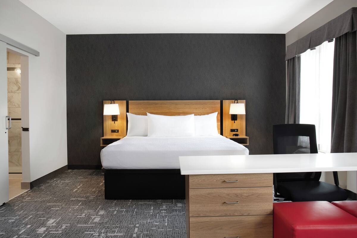 A hotel room with a bed, bedside lamps, a desk, and a chair.