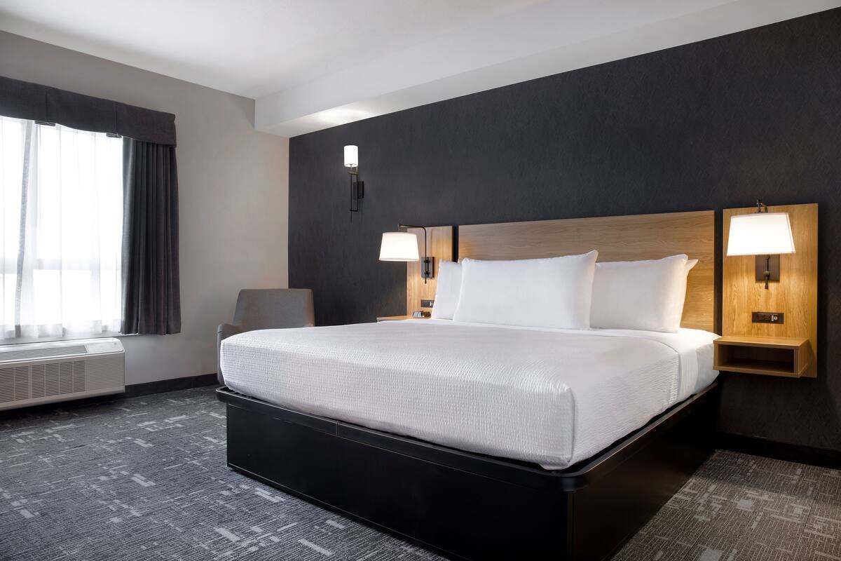 A hotel room with a large bed, two bedside lamps, a chair, and a window with curtains.