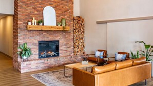 A modern living room with a brick fireplace, leather sofa, and a variety of plants. - Canalta Hotel Cochrane (Cochrane)